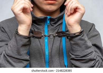 A teenage girl in handcuffs on a gray background. Juvenile delinquent, criminal liability of minors. Members of youth criminal groups and gangs. - Shutterstock ID 2148228385