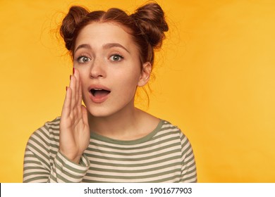 Teenage Girl, Happy Looking Red Hair Woman With Two Buns. Wearing Striped Blouse And Holding Hand Next To Her Mouth, Whisper To You. Watching At The Camera Isolated Over Yellow Background