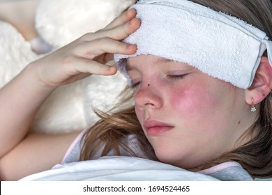 A Teenage Girl Has Flu Is Lying On Bed With Eyes Closed And Cold Compress For Headache. Viral Disease, Fever In Sick Person, Symptoms Of Respiratory Infection. High Temperature In Sleeping Young Woman