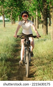 A Teenage Girl In A Helmet And Glasses Rides A Bicycle Along A Forest Path. Children's Cycling. Cycling Tourism.