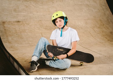 Teenage girl in helmet and stylish clothes posing on half pipe ramp an outdoor skate park. Beautiful kid female model skateboarder with skate board in urban extreme park. Schoolgirl after school. - Powered by Shutterstock