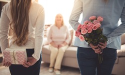Tizenéves Lány és Anyja Rejtőzik A Virágok és Egy Díszdoboz A Gyönyörű Nagyika Háta Mögött, Míg A Nagymama ül A Kanapén Otthon