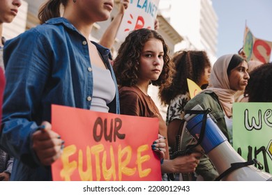 Teenage girl holding a megaphone while marching for climate justice with a group of demonstrators. Multicultural youth activists protesting against global warming and climate change. - Powered by Shutterstock