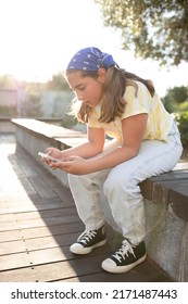 Teenage girl holding a mobile phone, sitting on a bench outdoors. Young woman chatting. Soft focus. concept of online, follower, social media, free time, passion for gadgets. Sunset