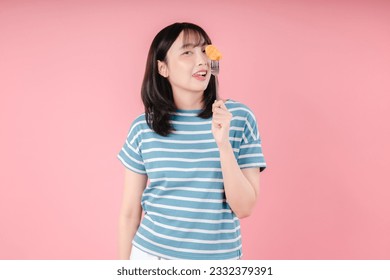 A teenage girl holds fork with nugget near her eyes isolated on pink background - Powered by Shutterstock