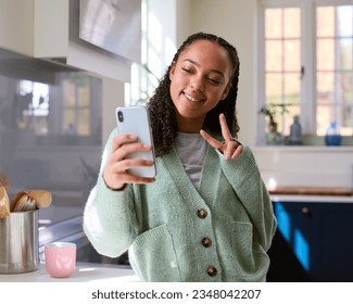 Teenage Girl At Home In Kitchen Posing For Selfie To Upload To Social Media On Mobile Phone - Powered by Shutterstock