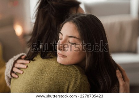 Teenage girl hugging her mother at home.