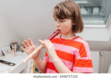 A teenage girl learns to play the flute and rehearses at home. Music school, music as a hobby for teenagers - Powered by Shutterstock