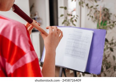 A teenage girl learns to play the flute and rehearses at home. Music school, music as a hobby for teenagers - Powered by Shutterstock