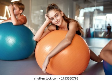 Teenage girl looking at camera while working out using exercise ball in gym. Sport, healthy lifestyle, physical education concept. Horizontal shot. Selective focus