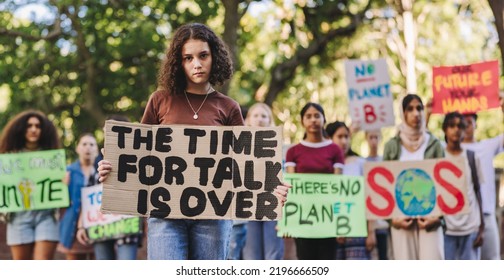 Teenage Girl Looking At The Camera While Leading A March Against Climate Change. Group Of Multiethnic Youth Activists Protesting Against Global Warming. Young People Joining The Global Climate Strike.