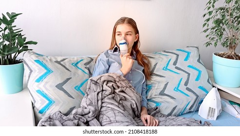 Teenage Girl Makes Inhalation With A Nebulizer Equipment. Sick Child Holding Inhalator In Hand And Breathes Through An Inhaler At Home. Physical Therapy For Cold, Flu And Broncial Asthma