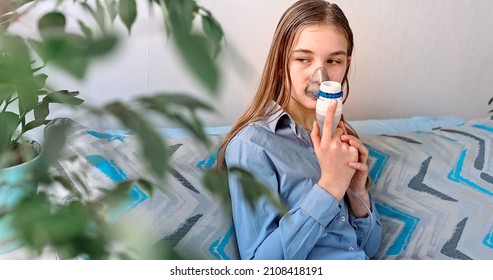 Teenage Girl Makes Inhalation With A Nebulizer Equipment. Sick Child Holding Inhalator In Hand And Breathes Through An Inhaler At Home. Physical Therapy For Cold, Flu And Broncial Asthma