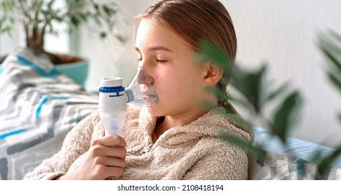 Teenage Girl Makes Inhalation With A Nebulizer Equipment. Sick Child Holding Inhalator In Hand And Breathes Through An Inhaler At Home. Physical Therapy For Cold, Flu And Broncial Asthma