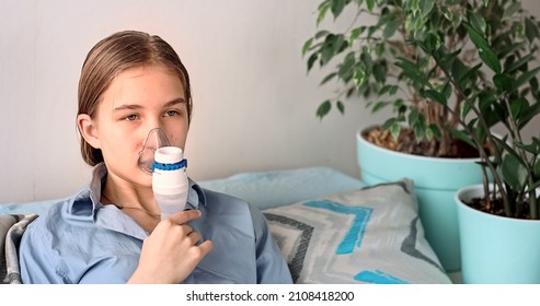 Teenage Girl Makes Inhalation With A Nebulizer Equipment. Sick Child Holding Inhalator In Hand And Breathes Through An Inhaler At Home. Physical Therapy For Cold, Flu And Broncial Asthma