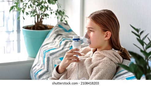 Teenage Girl Makes Inhalation With A Nebulizer Equipment. Sick Child Holding Inhalator In Hand And Breathes Through An Inhaler At Home. Physical Therapy For Cold, Flu And Broncial Asthma