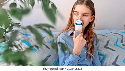 Teenage Girl Makes Inhalation With A Nebulizer Equipment. Sick Child Holding Inhalator In Hand And Breathes Through An Inhaler At Home. Physical Therapy For Cold, Flu And Broncial Asthma