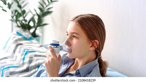 Teenage Girl Makes Inhalation With A Nebulizer Equipment. Sick Child Holding Inhalator In Hand And Breathes Through An Inhaler At Home. Physical Therapy For Cold, Flu And Broncial Asthma