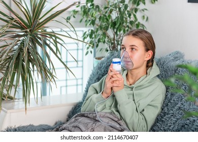 Teenage Girl Makes Inhalation With A Nebulizer Equipment. Sick Child Holding Inhalator In Hand And Breathes Through An Inhaler At Home. Physical Therapy For Cold, Flu And Bronchial Asthma