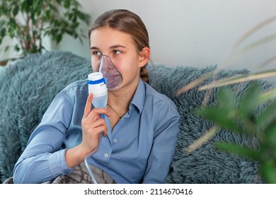 Teenage Girl Makes Inhalation With A Nebulizer Equipment. Sick Child Holding Inhalator In Hand And Breathes Through An Inhaler At Home. Physical Therapy For Cold, Flu And Bronchial Asthma