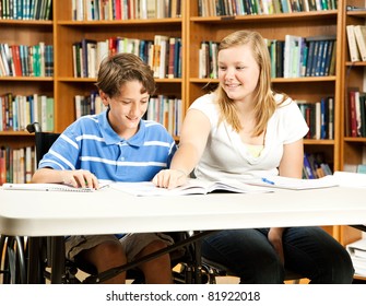 Teenage Girl Mentoring A Younger, Disabled Boy In The School Library.