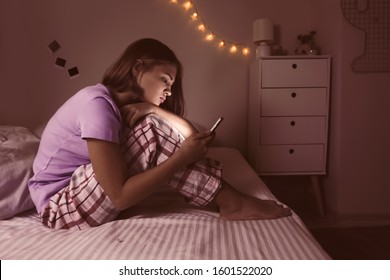 Teenage Girl With Mobile Phone In Bedroom At Night