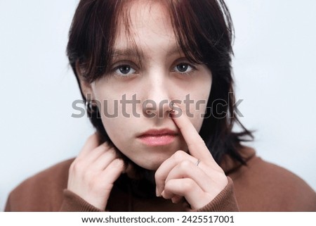 A teenage girl needs more attention from her parents, she has few friends and is often sad. Teenage girl with acne on her face and nose piercing is sad, skin care, close up