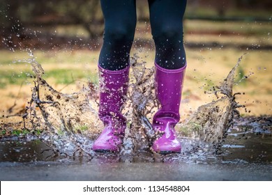 Teenage girl photographed from the waist down wearing black leggings and purple rain boots and splashing in a mud puddle - Powered by Shutterstock