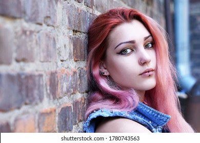 Teenage girl with pink hair sitting against brick wall in the background.