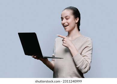 Teenage girl pointing finger at laptop monitor, gray background - Shutterstock ID 2311240999