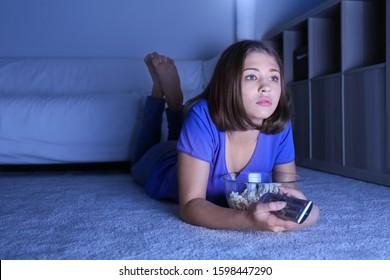 Teenage girl with popcorn watching TV at home late in evening
