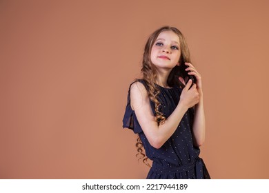 Teenage Girl Princess 10 Year Old With Curly Long Hair Call On Mobile Phone At Beige Background, Talking And Looking. Fashion Model In Stylish Blue Dress. Fashionable Young Lady Model. Copy Text Space