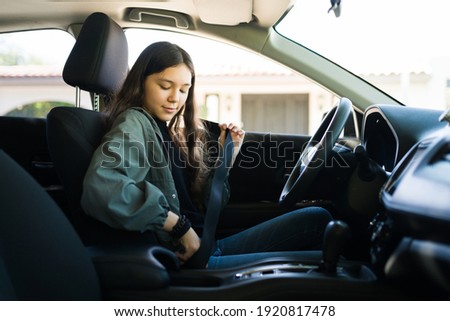 Teenage girl putting on her safety seatbelt and about to start the car. Teen driver getting ready to drive her new car