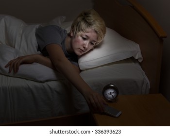 Teenage Girl Reaching For Her Cell Phone, On Night Stand, While In Bed. Teen Using Technology Late At Night Instead Of Sleeping. 