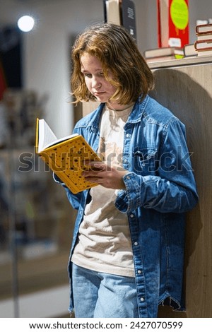 Teenage girl reading the book in large bookshop of London