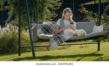 A teenage girl is resting on a garden swing, using a smartphone - Shutterstock ID 2364996203