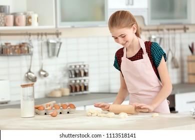 Teenage girl rolling dough on table in kitchen