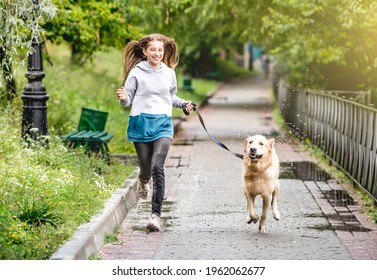 Teenage Girl Running With Golden Retriever Dog In Park After Rain