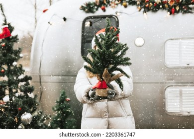 teenage girl in Santa hat stands with Christmas tree on Christmas morning and celebrate New Year or Christmas outdoor near trailer mobile home recreational vehicle, local travel