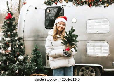 Teenage Girl In Santa Hat Stands With Christmas Tree On Christmas Morning And Celebrate New Year Or Christmas Outdoor Near Trailer Mobile Home Recreational Vehicle, Local Travel