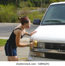 Teenage girl scrubs van headlight with a sponge