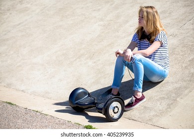 A Teenage Girl Sitting With Her Hoverboard At His Feet