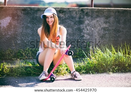 A teenage girl sitting on a curb. She holds her skateboard and smiles. Perfect summer sunlight.