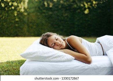 Teenage Girl Sleeping On Soft Mattress And Pillow On Grass Outside. Healthy Relaxing On Cosy Bed On Fresh Air In Garden.