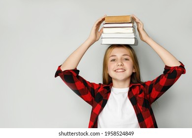 A teenage girl with a smile holds a lot of books on her head, the joy of education. Receive knowledge with joy.