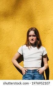 Teenage Girl Standing Next To The Yellow Concrete Wall. Candid Portrait In Sunny Day. City Street Life Authentic People. Young Female In Urban Outfit