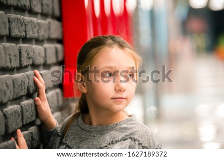 A teenage girl stands by a brick wall and looks away