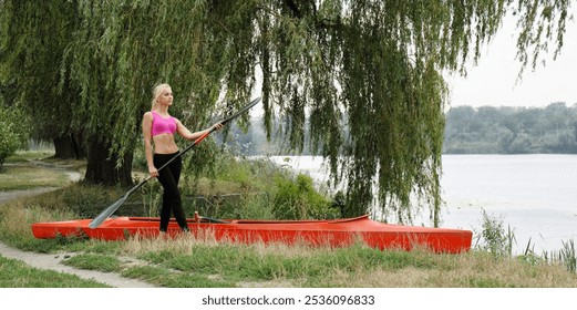 A teenage girl stands near a red kayak and holds an oar in her hand. Concept of physical and mental health of teenagers - Powered by Shutterstock