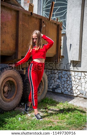  teenage girl stands in a sport suit near an old car against a ruined building, the concept of a youth life style