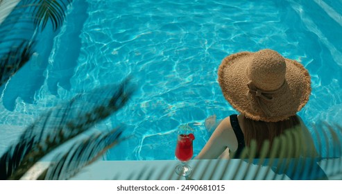 Teenage girl in a straw hat relaxing by the pool, with palm leaves swaying in the foreground - Powered by Shutterstock